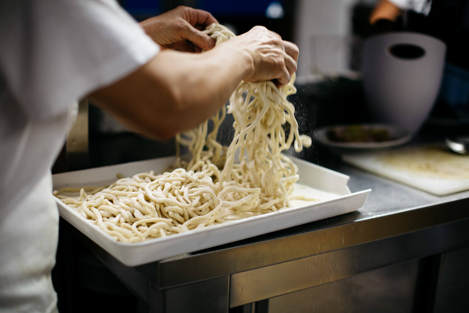 cook adding flour to spaghetti in a tray